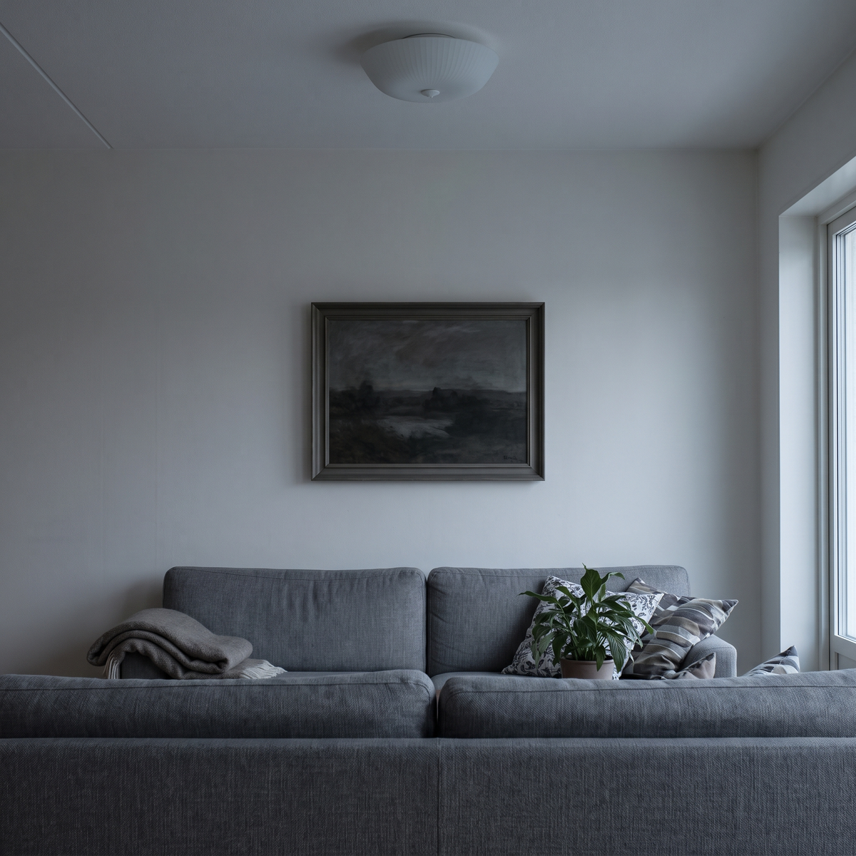 Billedet over sofaen i fladt loftslys en novembereftermiddag – farverne er grå